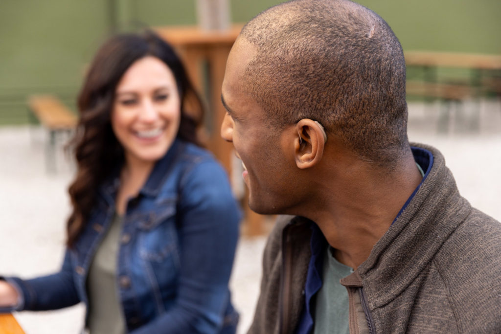 grown man at a picnic table smiling showing his almost invisible hearing aids from Injoy