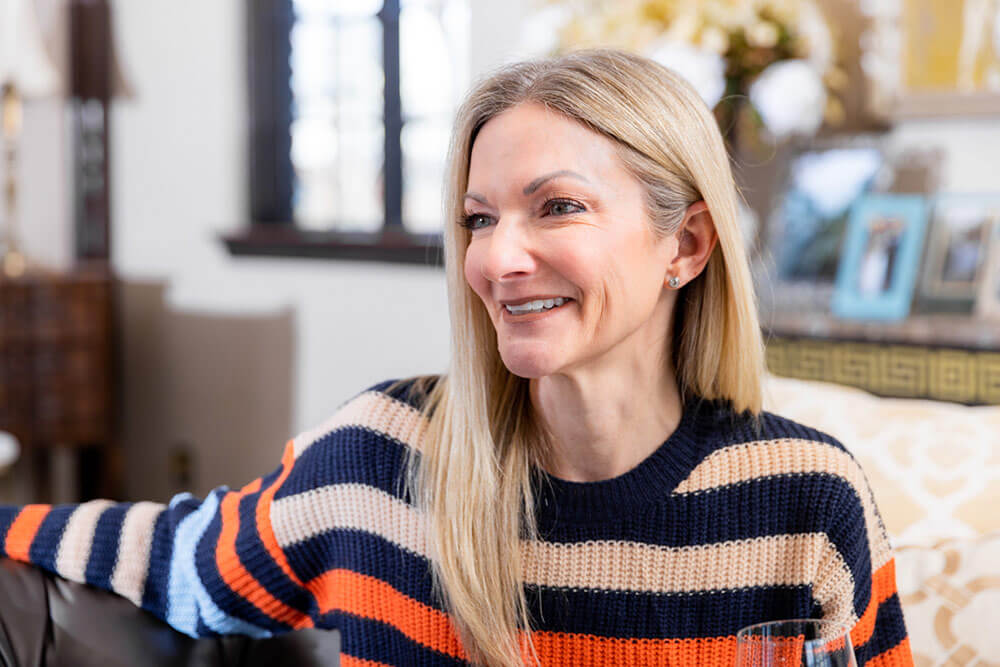 A middle-aged woman smiles while sitting and holding a glass. 