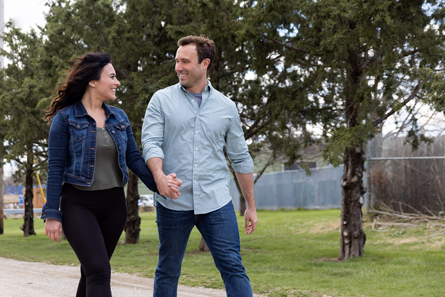 A couple holding hands walks in a park.