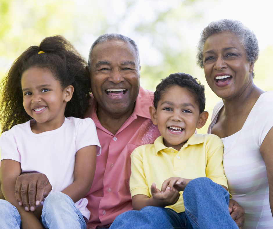 Happy grandparents sit outside with their two smiling grandchildren.