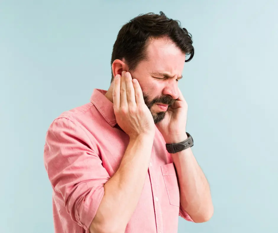 A man holds his ears and grimaces. 