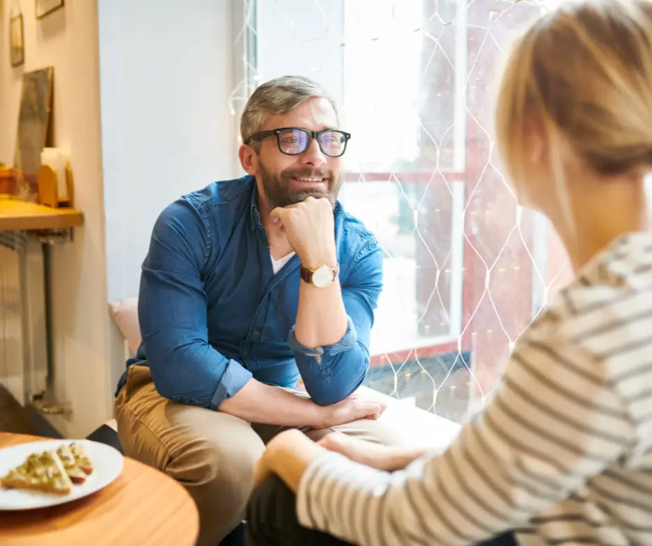 A man smiles at a woman as she speaks during their lunch. 