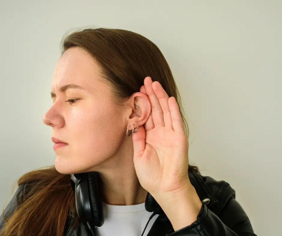 A woman cups her hand around her ear. 